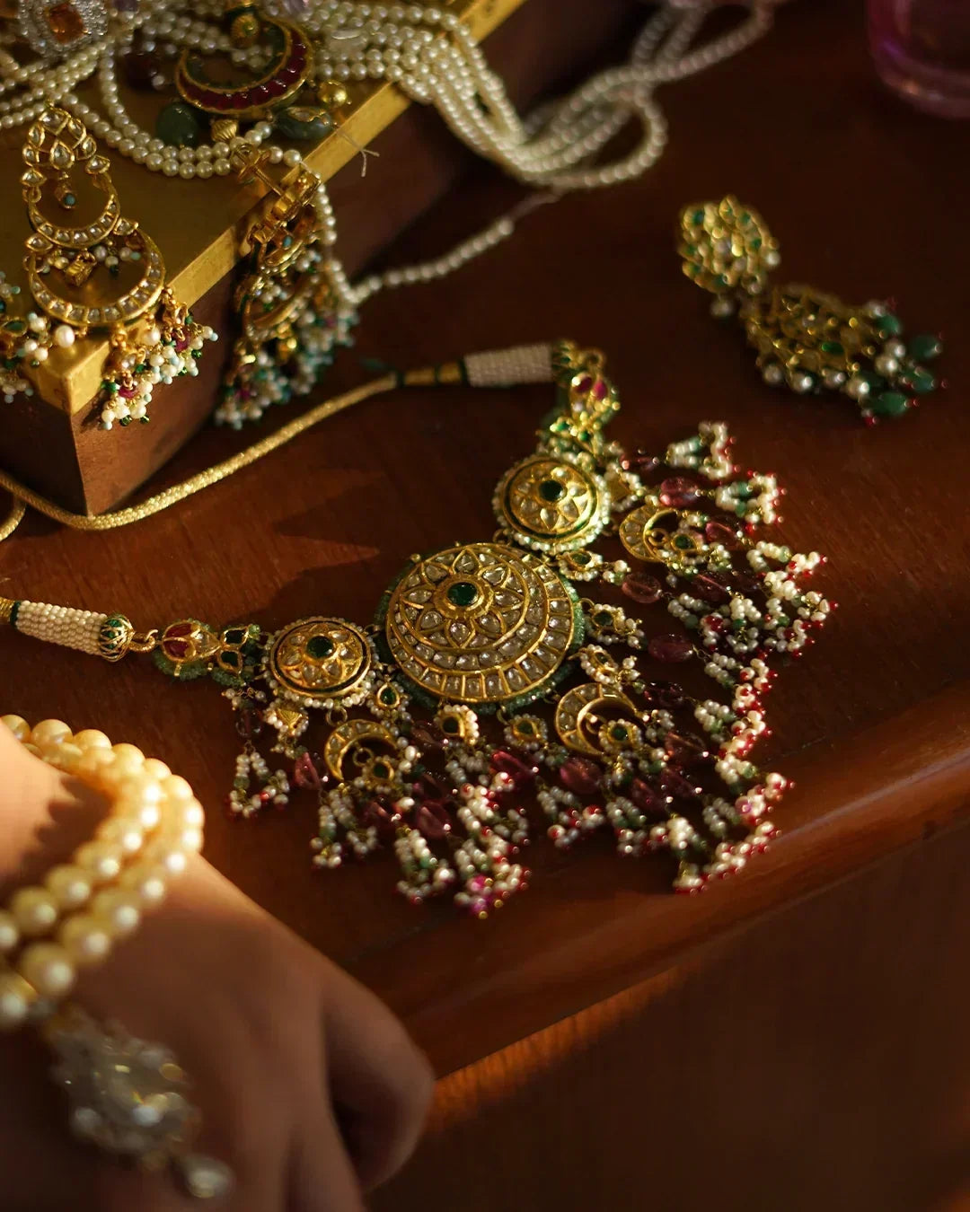Gold choker necklace with kundan-set polki diamonds, rosette and crescent motifs, emerald beads, pearl fringes, and gemstone tassels.