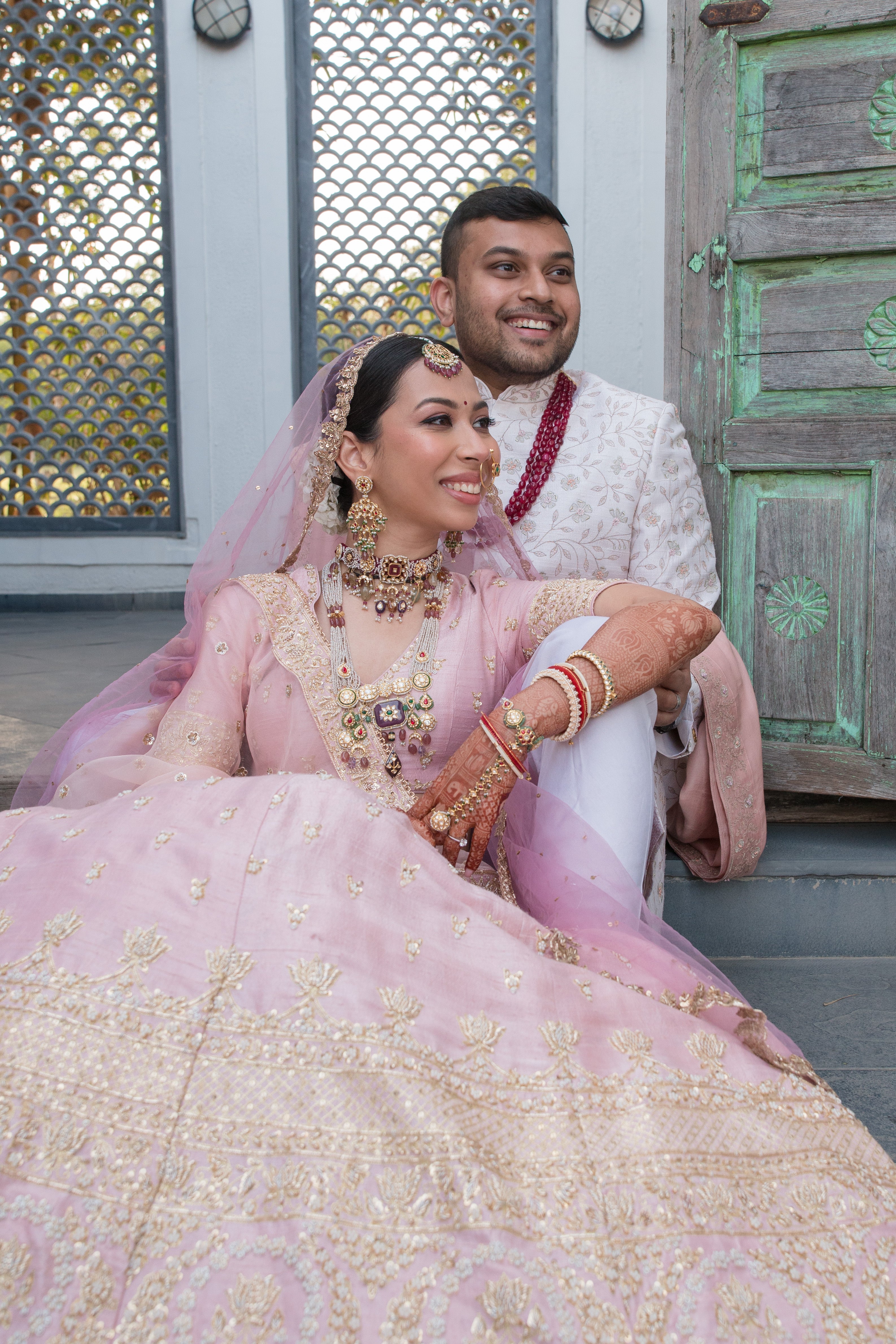 A bride and groom seated together during their wedding celebrations, with the bride wearing bespoke Aurus bridal jewellery featuring layered polki necklaces, a maang tikka, earrings, and bangles.