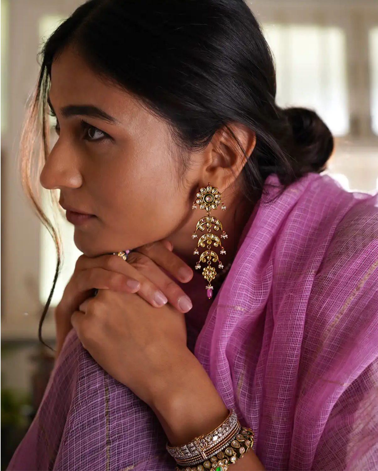 Model image wearing handcrafted gold lasya chandelier earrings featuring a floral rosette top, layered crescent motifs, kundan-set polki (uncut) diamonds, coloured gemstones, red enamel accents, and seed pearl fringes