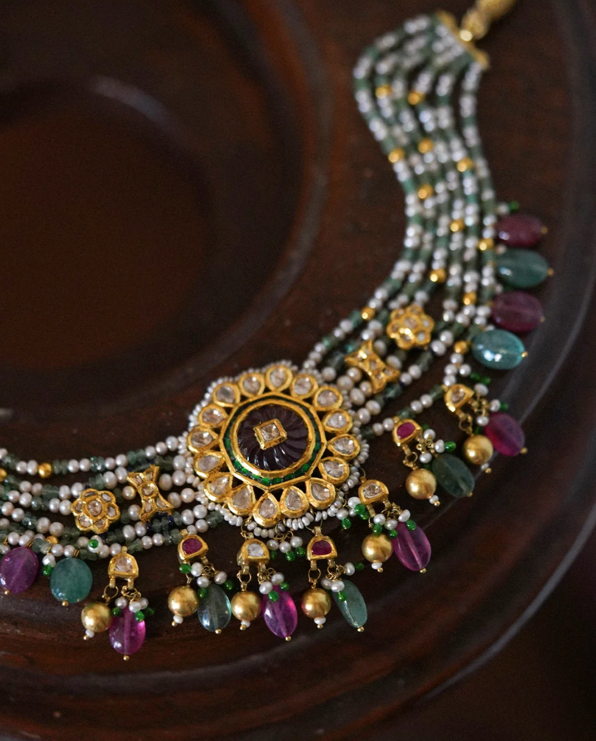 Handcrafted Vanya gold choker featuring parallel strands of cultured pearls, kundan-set polki (uncut) diamonds, a central floral rosette with carved tourmaline, green enamel accents, and tourmaline drop details.