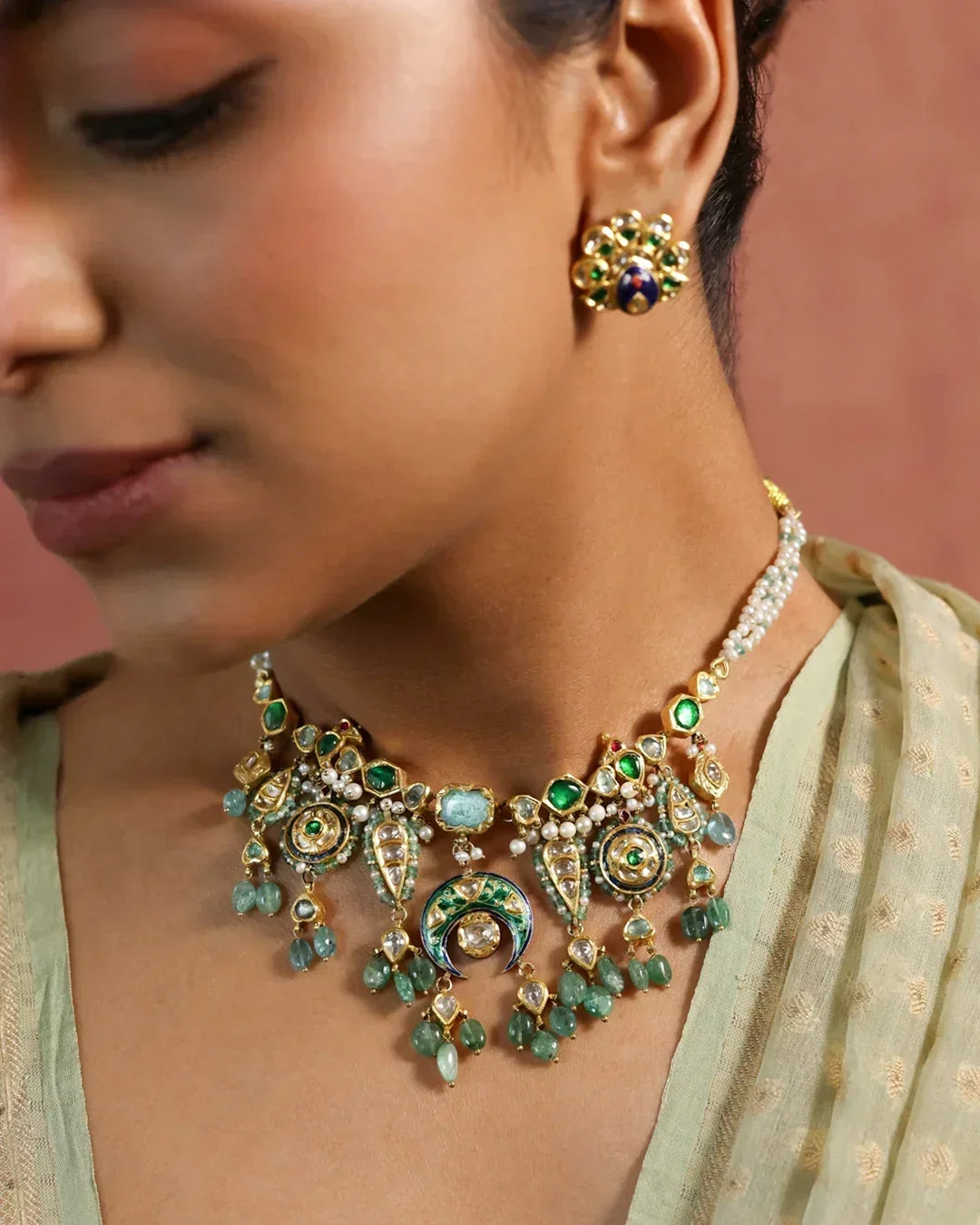 Model wearing the handcrafted Viana gold necklace featuring a green enamel crescent centerpiece with polki diamonds, emeralds, and cultured pearls.