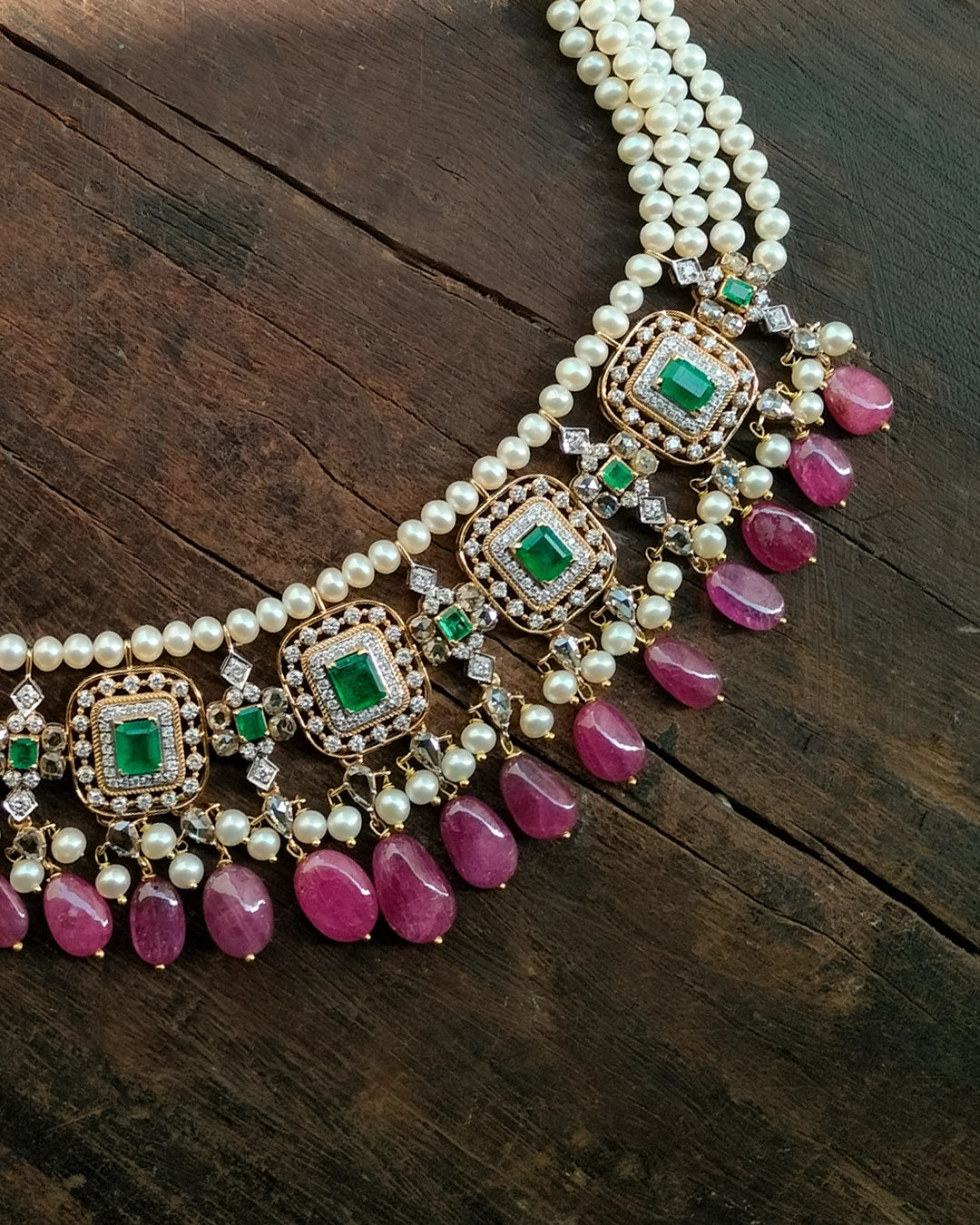 Aesha Necklace in gold featuring emerald-set square motifs framed in brilliant-cut diamonds, pearl strands, and a cultured pearl and ruby drop fringe