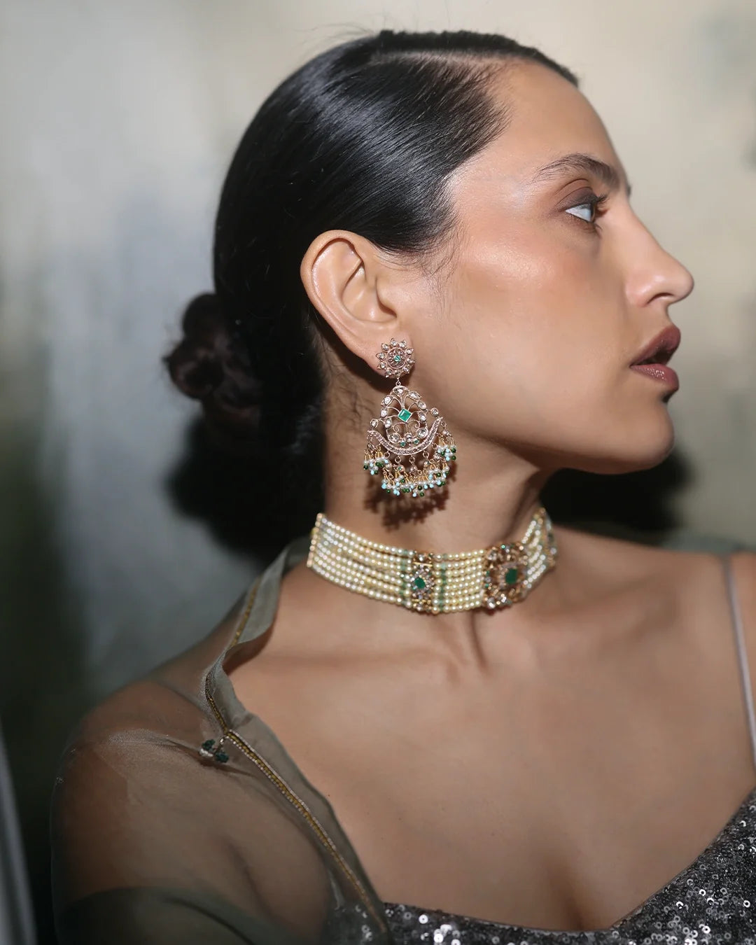 Woman wearing Nehir gold earrings featuring diamonds, emeralds, and cultured pearls