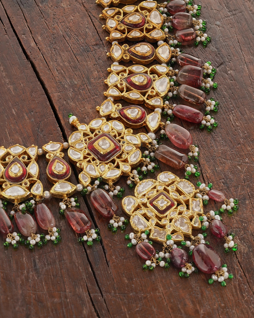 Rati gold polki necklace with uncut diamonds, wine-hued tourmaline drops, cultured pearls, green enamel accents, and intricate red meena work in a statement bridal jewellery design.